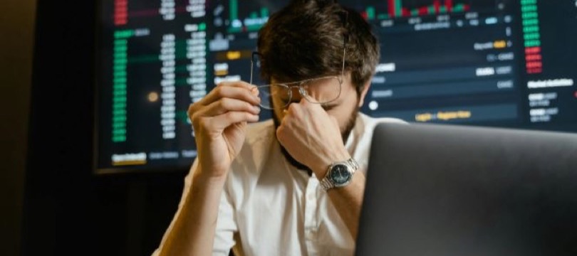 Stressed trader pinching the bridge of his nose in front of falling market charts