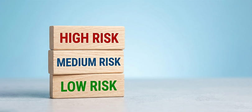 Three stacked wooden blocks reading HIGH RISK, MEDIUM RISK and LOW RISK against a light blue background