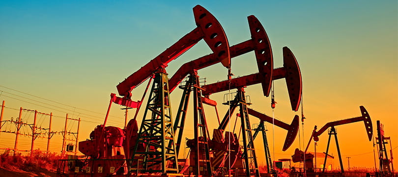 Oil pumpjacks silhouetted against an orange sky at sunset