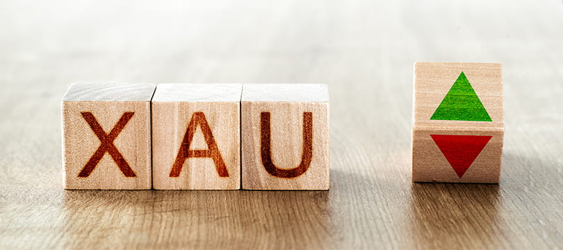 Wooden blocks spelling XAU with green and red arrows, the ticker for spot gold