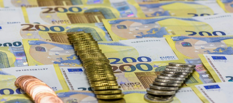 Stacks of euro coins of different heights, one tall stack of gold-colored coins and a short stack of silver-colored coins, standing on a spread of 200-euro banknotes