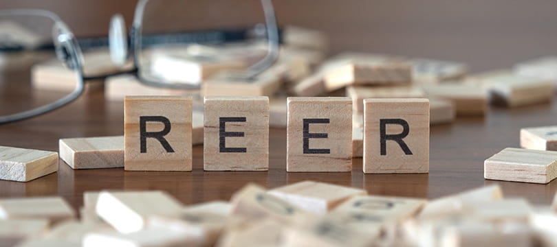 Wooden letter tiles spelling REER on a table, with reading glasses in the background