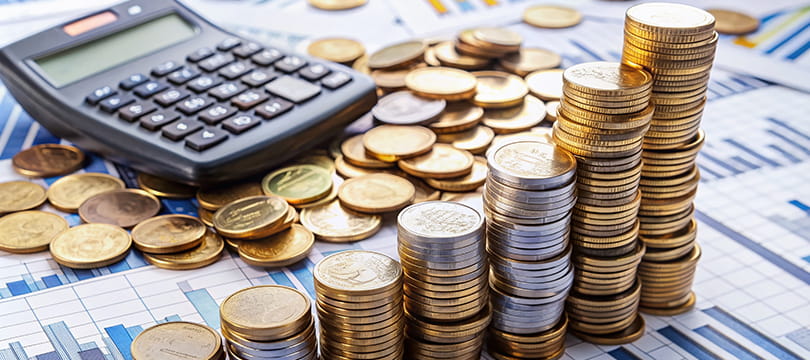 Stacks of gold and silver coins and a calculator on printed financial charts