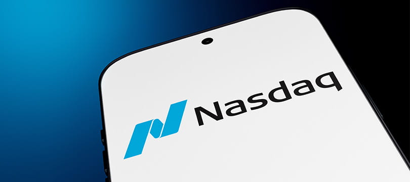 Nasdaq logo on a smartphone screen in front of a trading chart